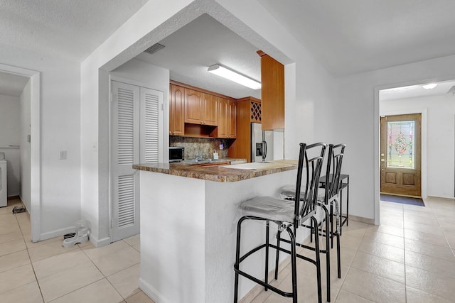 kitchen featuring a breakfast bar, tasteful backsplash, a peninsula, appliances with stainless steel finishes, and light tile patterned floors