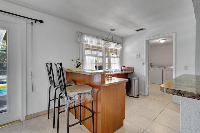 10476 SW 52nd St, Cooper City, FL 33328 - kitchen featuring separate washer and dryer, a peninsula, light tile patterned flooring, a kitchen bar, and decorative light fixtures
