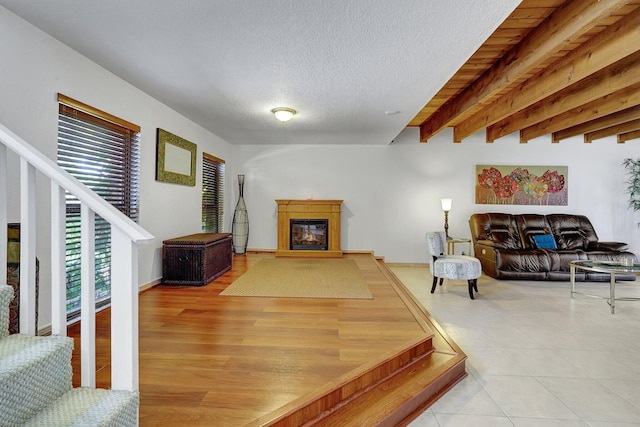 living area with stairway, light tile patterned flooring, a textured ceiling, a glass covered fireplace, and beamed ceiling