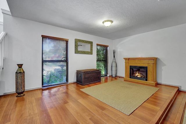 interior space with a glass covered fireplace, a textured ceiling, baseboards, and wood finished floors