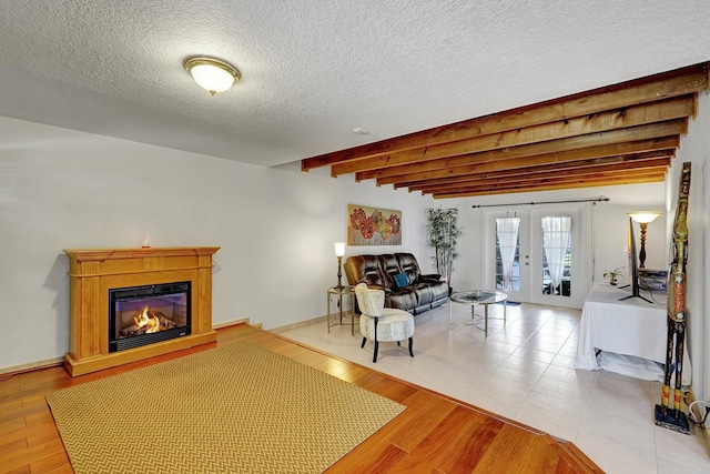 living room featuring a glass covered fireplace, beam ceiling, wood finished floors, and french doors