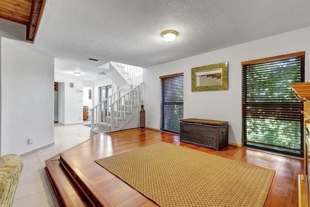 interior space featuring visible vents, light wood-style flooring, a textured ceiling, baseboards, and stairs