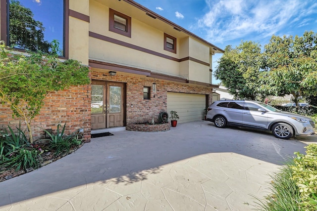 rear view of house with brick siding, stucco siding, an attached garage, and driveway