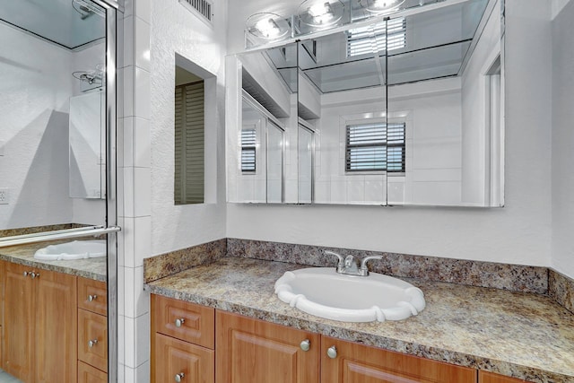 full bath featuring vanity, an enclosed shower, a textured wall, and visible vents