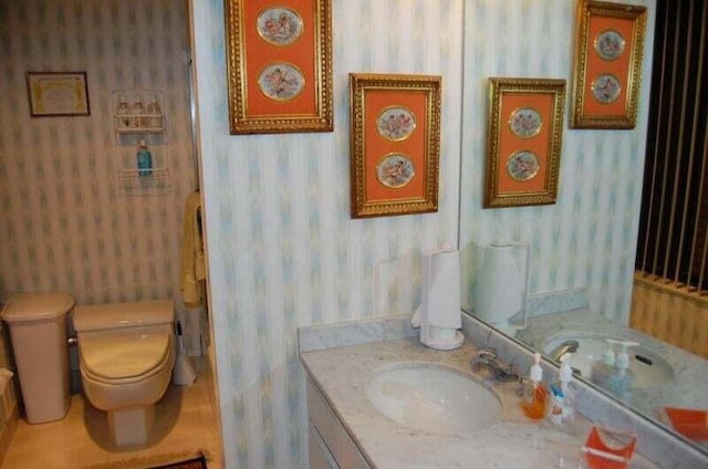 bathroom featuring toilet, vanity, and wallpapered walls