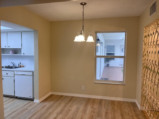 unfurnished dining area featuring light wood finished floors, visible vents, baseboards, a chandelier, and a sink