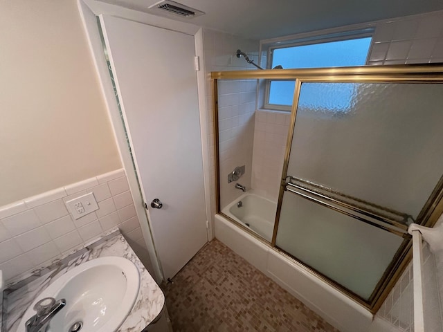 full bathroom with visible vents, bath / shower combo with glass door, wainscoting, tile walls, and a sink