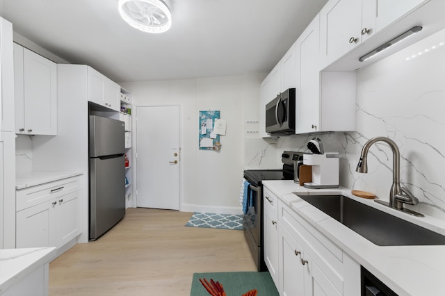 kitchen featuring light stone countertops, a sink, decorative backsplash, appliances with stainless steel finishes, and white cabinetry