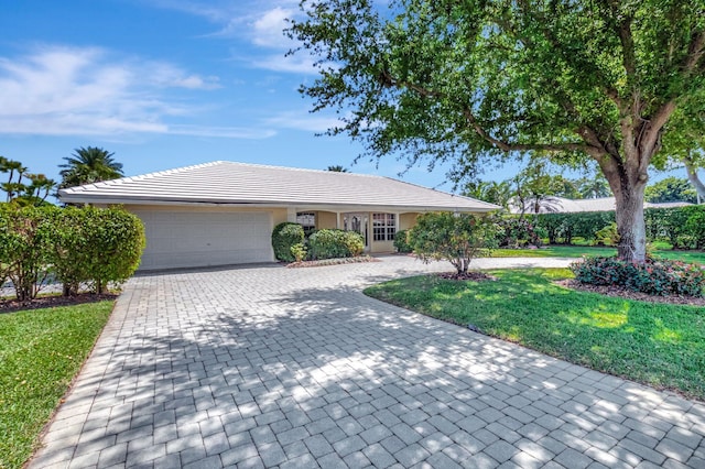 ranch-style house featuring a front lawn, a tiled roof, stucco siding, decorative driveway, and a garage