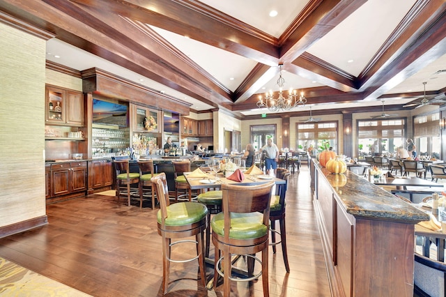 dining space with beam ceiling, ornamental molding, ceiling fan with notable chandelier, hardwood / wood-style flooring, and coffered ceiling