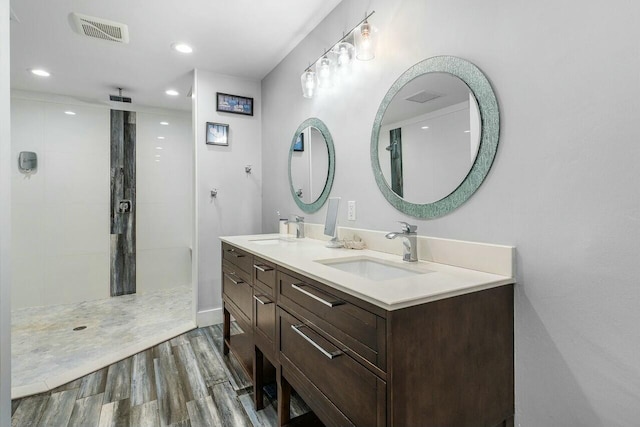 full bathroom featuring wood finished floors, a sink, a tile shower, and visible vents