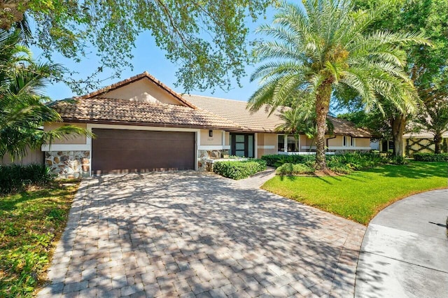 single story home with a tile roof, a front yard, stucco siding, decorative driveway, and a garage