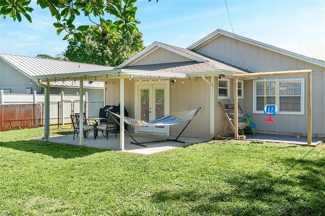 rear view of property featuring fence, french doors, a yard, roof with shingles, and a patio area