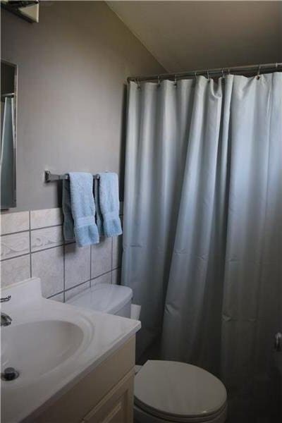 full bath featuring vanity, tile walls, toilet, and vaulted ceiling