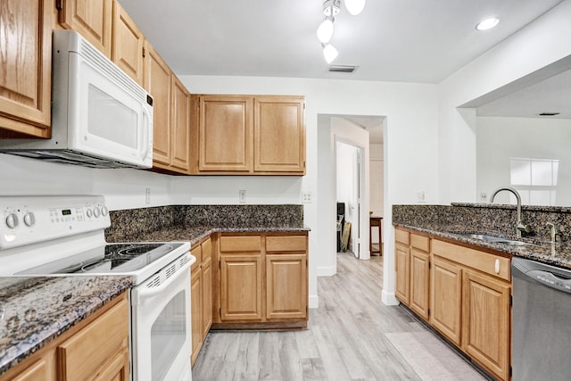 kitchen featuring a sink, visible vents, white appliances, and dark stone counters