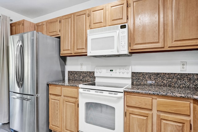 kitchen with light brown cabinets, dark stone countertops, and white appliances