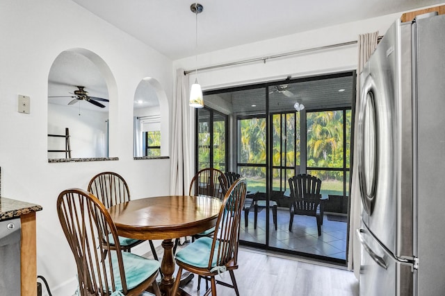 dining space with arched walkways, a ceiling fan, and wood finished floors