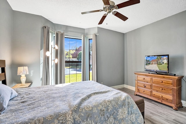 bedroom with ceiling fan, a textured ceiling, baseboards, and wood finished floors