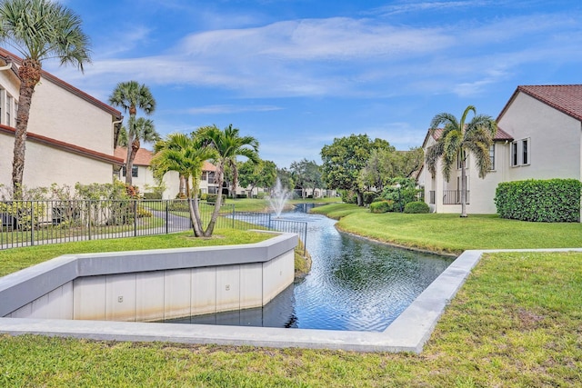 view of property's community with a water view, a lawn, and fence