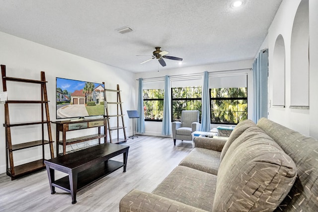 living room featuring arched walkways, visible vents, light wood-style floors, and a ceiling fan