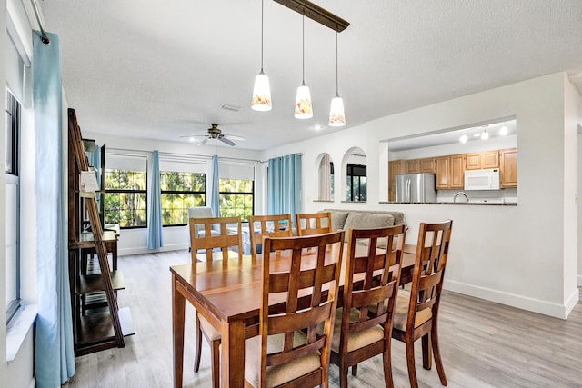 dining space with a textured ceiling, light wood-style flooring, baseboards, and ceiling fan