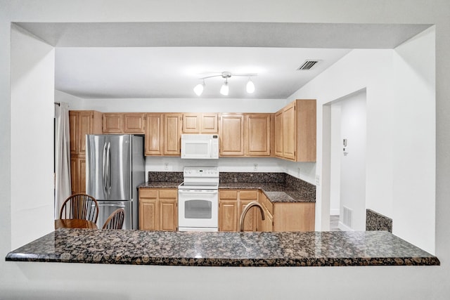 kitchen featuring white appliances, dark stone counters, visible vents, and a sink