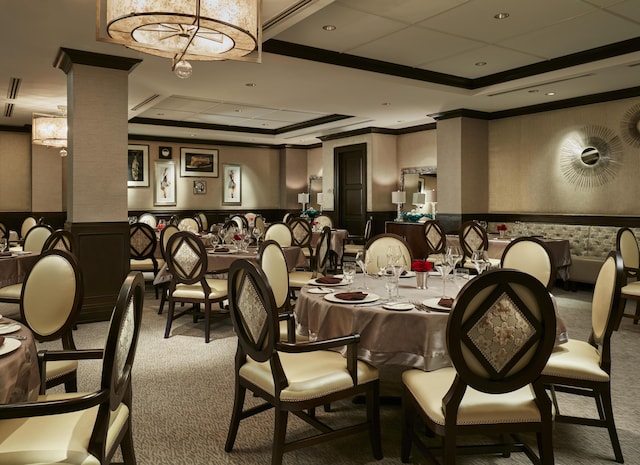 carpeted dining room with a raised ceiling, wallpapered walls, crown molding, and wainscoting