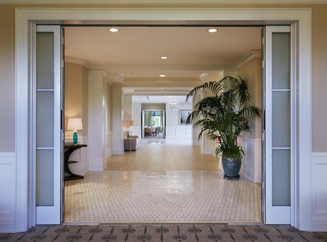 corridor with a wainscoted wall, recessed lighting, crown molding, and a decorative wall