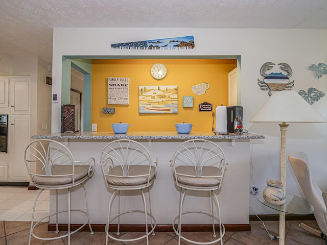 interior space featuring a textured ceiling, light tile patterned floors, baseboards, and oven