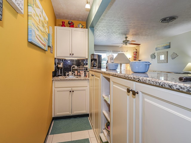 kitchen with light tile patterned floors, visible vents, ceiling fan, a sink, and a textured ceiling