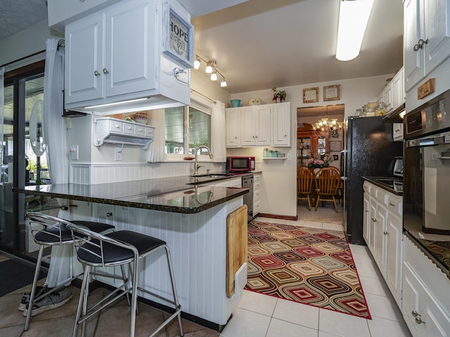 kitchen featuring black oven, a breakfast bar area, a peninsula, an inviting chandelier, and a sink