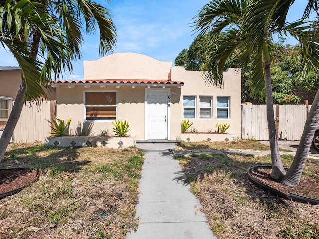 mediterranean / spanish-style house featuring fence, stucco siding, and a tile roof
