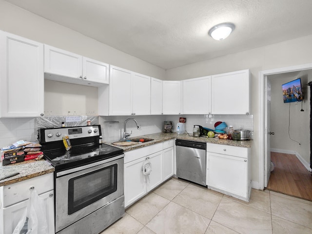 kitchen with a sink, decorative backsplash, light stone counters, white cabinetry, and appliances with stainless steel finishes