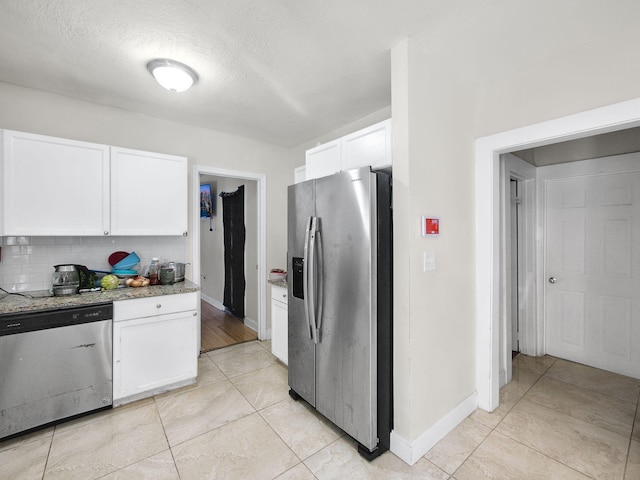 kitchen featuring tasteful backsplash, light stone counters, appliances with stainless steel finishes, white cabinets, and baseboards