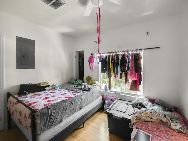 bedroom featuring a ceiling fan, electric panel, wood finished floors, and visible vents