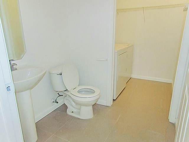 bathroom with baseboards, toilet, tile patterned flooring, and washing machine and clothes dryer