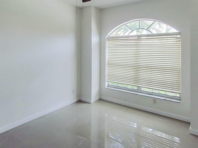 unfurnished room with a healthy amount of sunlight, a ceiling fan, and baseboards