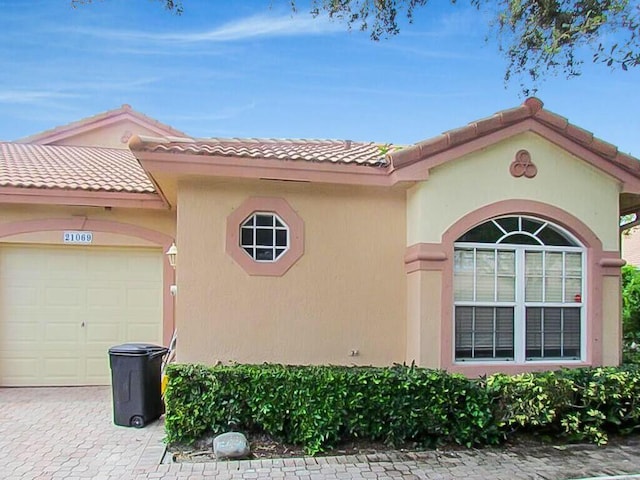 view of home's exterior with decorative driveway, stucco siding, an attached garage, and a tiled roof