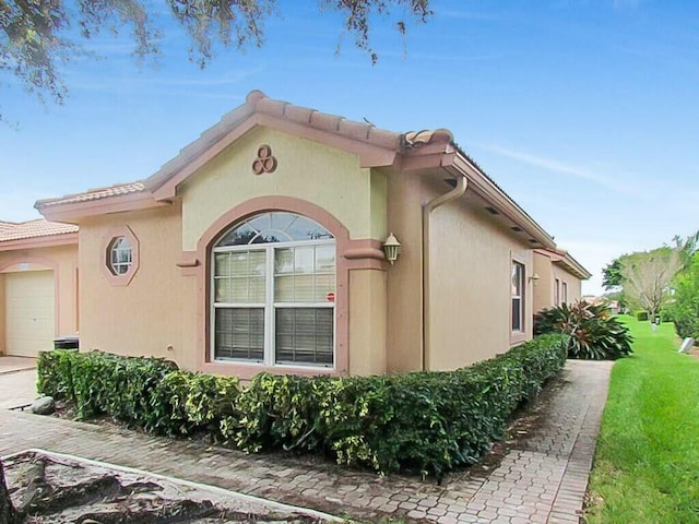 view of home's exterior featuring a tiled roof, an attached garage, and stucco siding