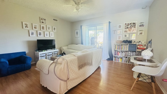 living area with wood finished floors, a ceiling fan, visible vents, and a textured ceiling