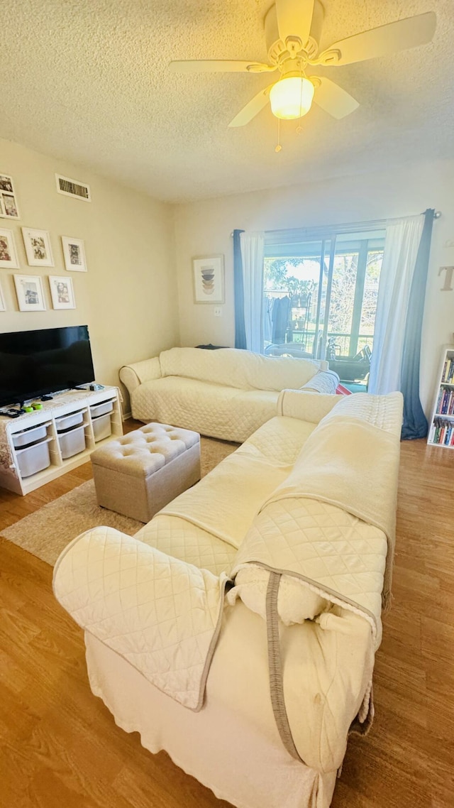 living room with visible vents, a textured ceiling, a ceiling fan, and wood finished floors