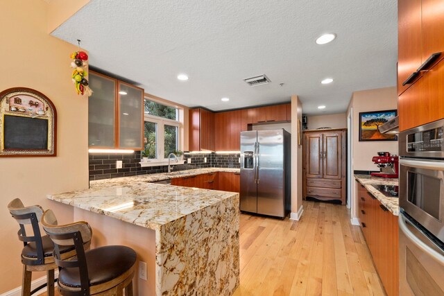 309 E Ocean Ave Unit 103, Lantana, FL 33462 - kitchen with decorative backsplash, a peninsula, stainless steel appliances, light wood-style floors, and light stone counters