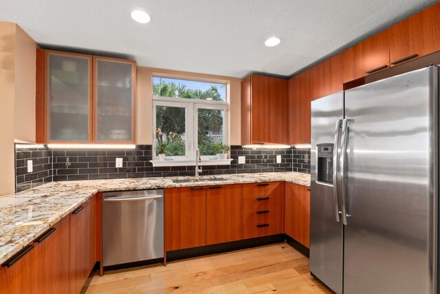 309 E Ocean Ave Unit 103, Lantana, FL 33462 - kitchen with light wood finished floors, light stone countertops, stainless steel appliances, a sink, and brown cabinetry