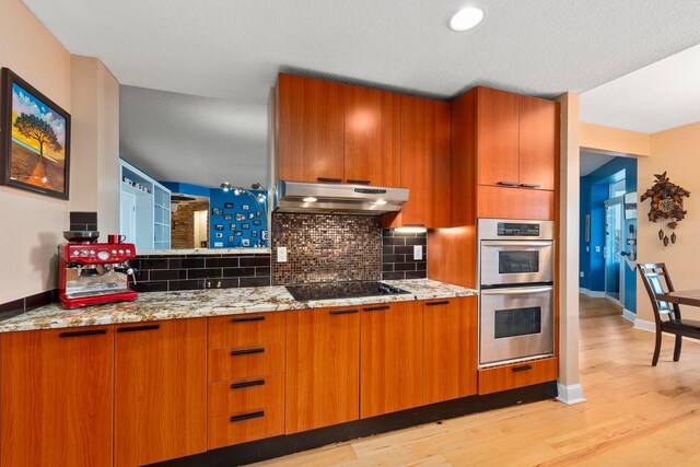 309 E Ocean Ave Unit 103, Lantana, FL 33462 - kitchen featuring tasteful backsplash, under cabinet range hood, black electric stovetop, double oven, and brown cabinetry