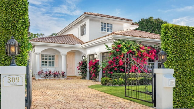 mediterranean / spanish home with stucco siding, a tiled roof, decorative driveway, and a gate