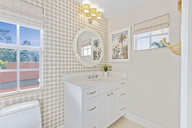 bathroom with baseboards, toilet, vanity, and wallpapered walls