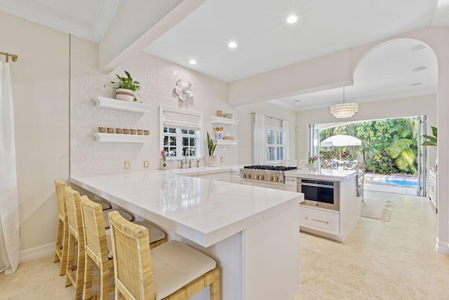 kitchen with ornamental molding, light stone counters, a peninsula, white cabinetry, and open shelves