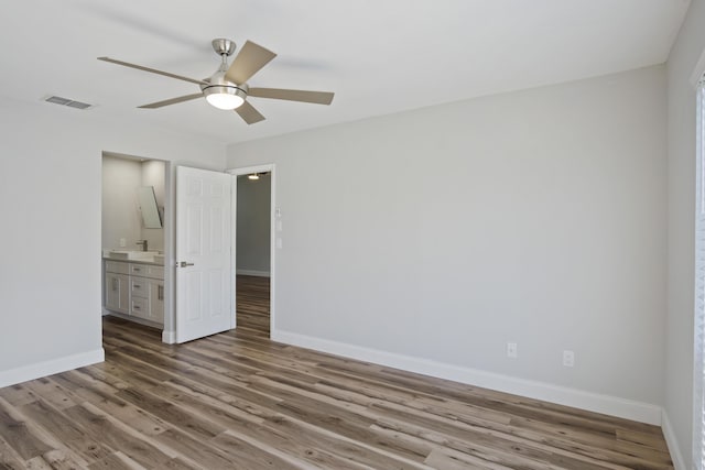 unfurnished bedroom with visible vents, baseboards, ensuite bathroom, wood finished floors, and a ceiling fan