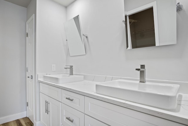 full bathroom featuring double vanity, wood finished floors, baseboards, and a sink