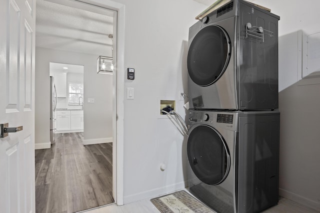 laundry area with laundry area, wood finished floors, stacked washer and clothes dryer, and baseboards